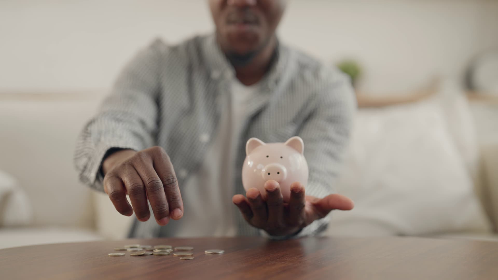 Young man putting coins in piggy bank at home