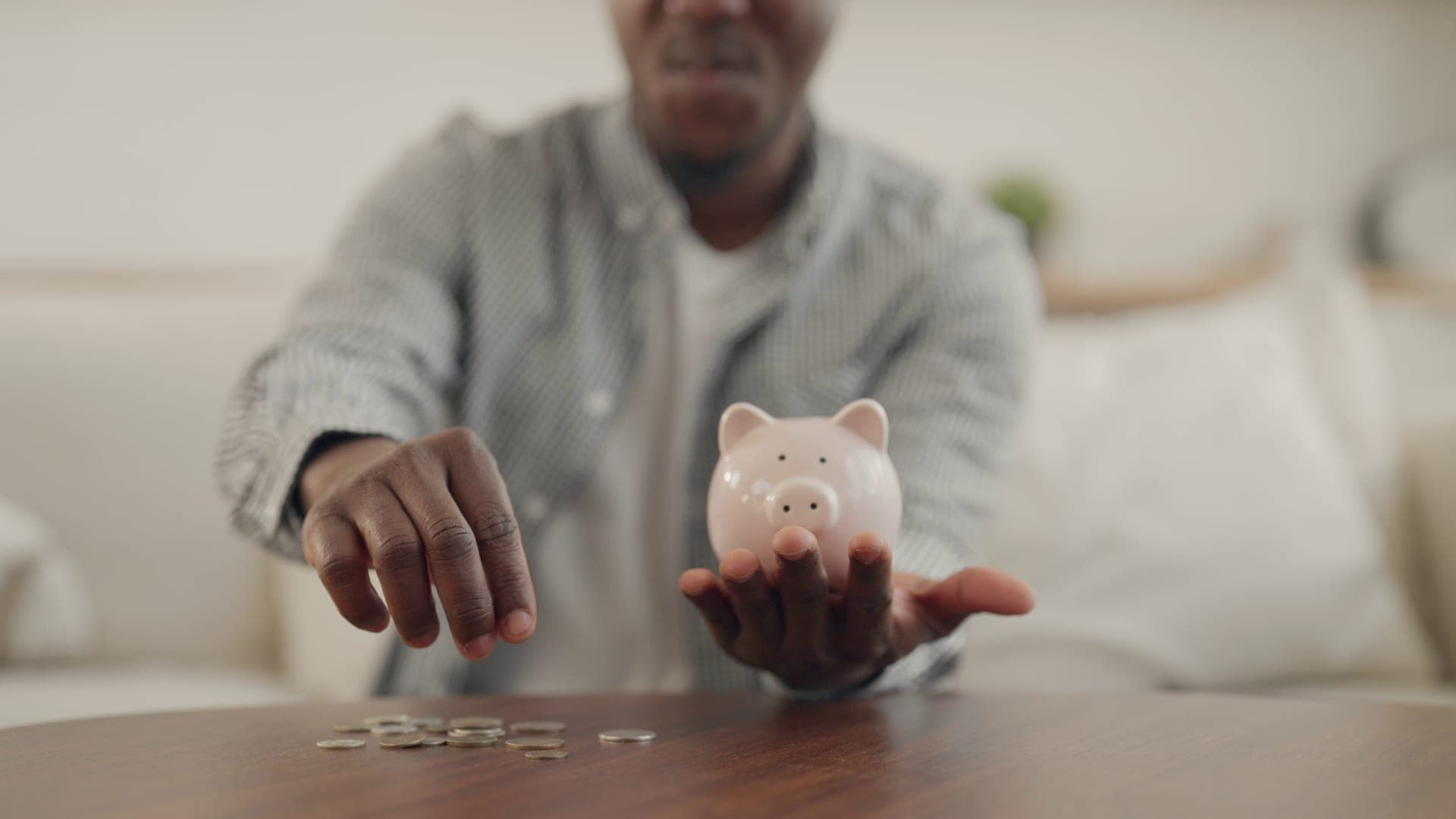 Young man putting coins in piggy bank at home